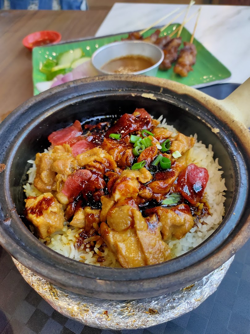 A close-up of delicious claypot chicken rice with Chinese sausage, served with satay in the background.