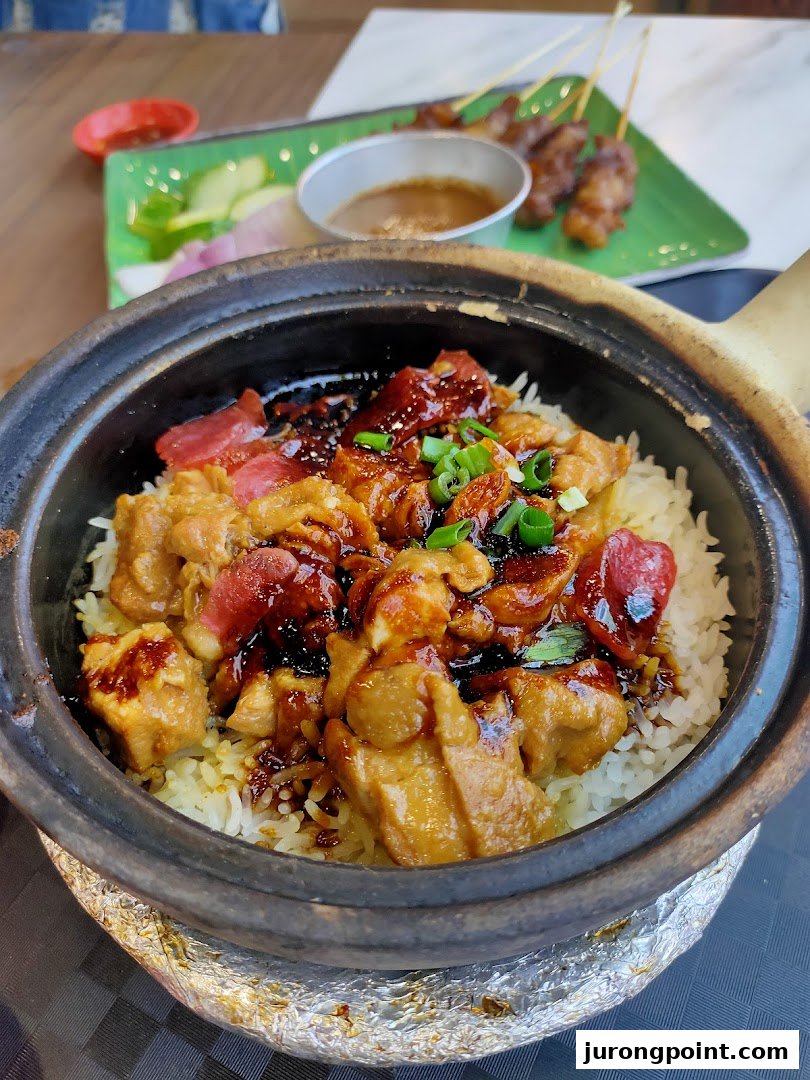 A close-up of delicious claypot chicken rice with Chinese sausage, served with satay in the background.
