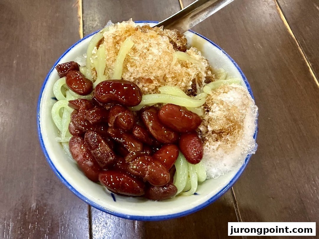 A vibrant bowl of traditional Malaysian dessert with red beans, green cendol, and shaved ice.