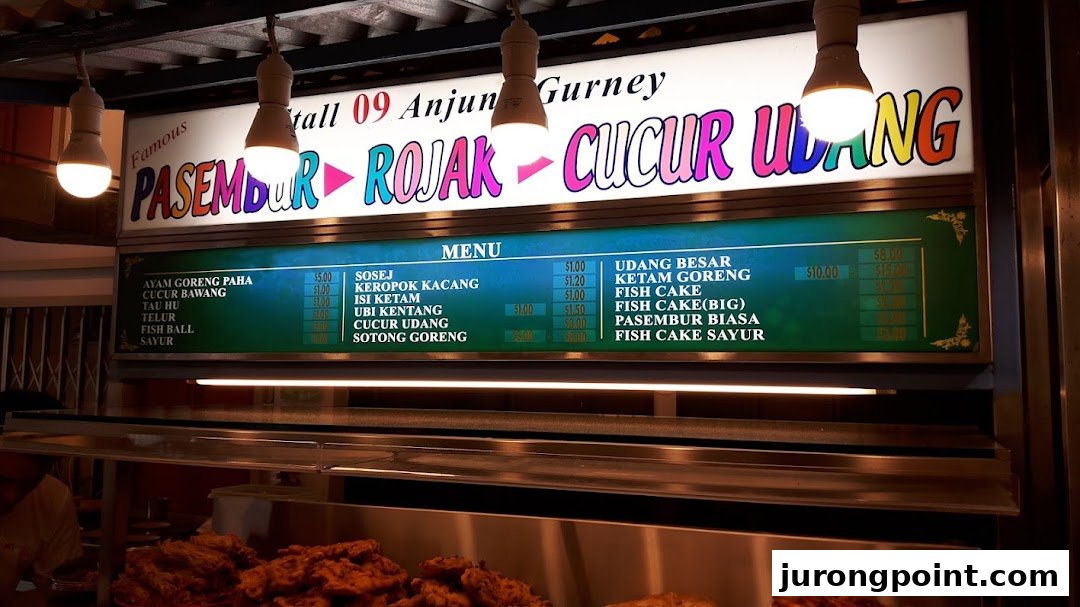A brightly lit menu board displaying various Malaysian fritters, snacks, and dishes with prices.