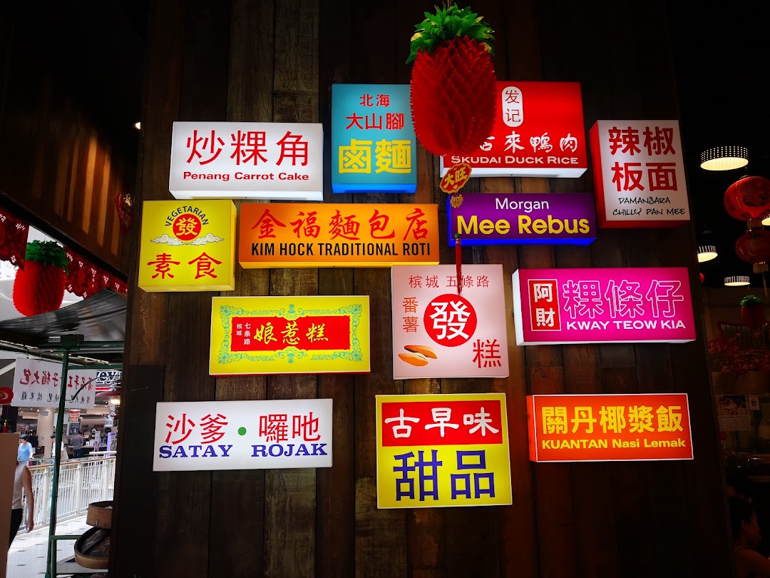 Illuminated signs showcasing various Malaysian hawker dishes on a rustic wooden wall.