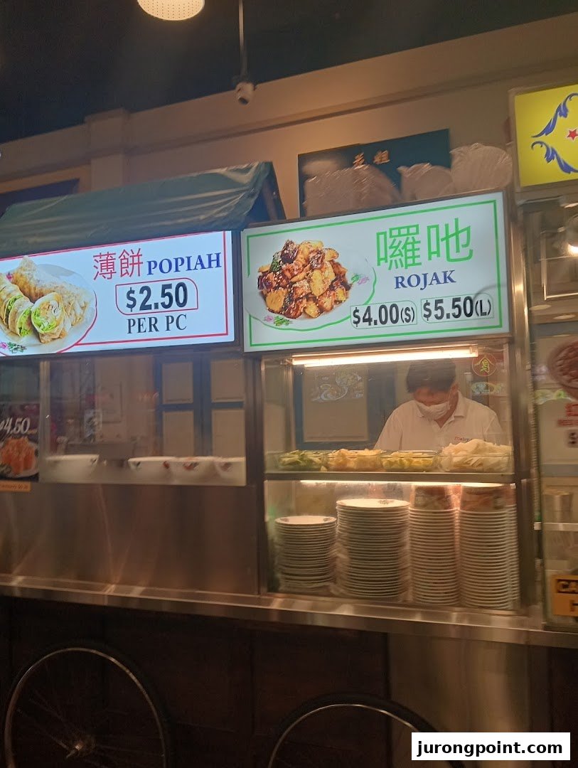 A food stall counter at Malaysia Boleh! displaying menu items like Popiah and Rojak with prices.