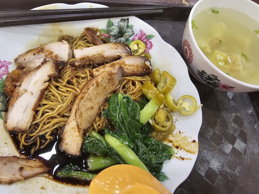 A delicious plate of wanton mee with char siew, green vegetables, pickled chilies, and a side of soup.