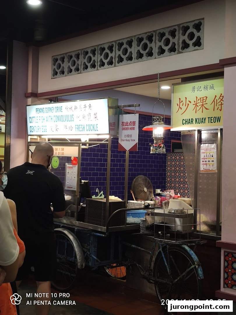 A bustling food stall at Malaysia Boleh! featuring a chef preparing Char Kuay Teow on a vintage bicycle cart.