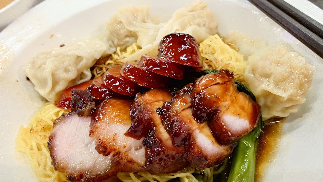 A close-up of a delicious plate of char siu wonton noodles with bok choy.