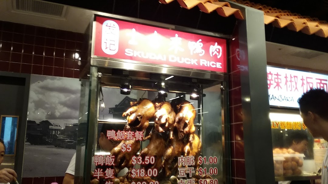 A food stall displaying roasted ducks and a menu with prices for duck rice and side dishes.