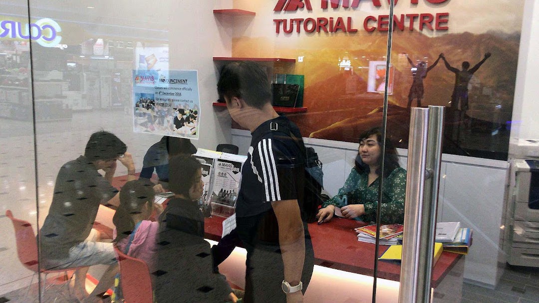 Students and staff inside Mavis Tutorial Centre, visible through a glass partition, engaged in learning activities.