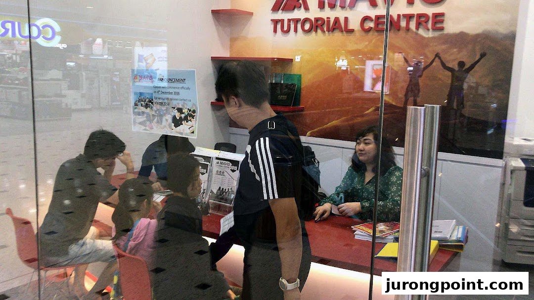 Students and staff inside Mavis Tutorial Centre, visible through a glass partition, engaged in learning activities.
