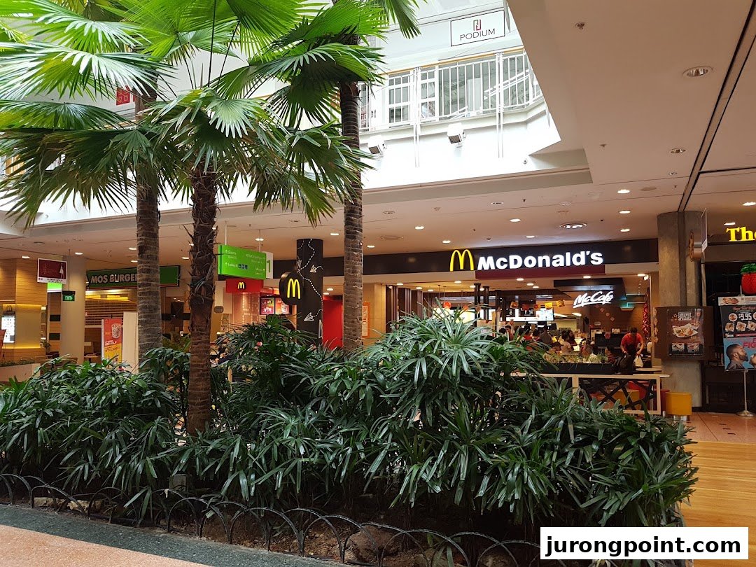 The McDonald's shop front in a mall, featuring its iconic logo and a McCafé section, surrounded by indoor greenery.