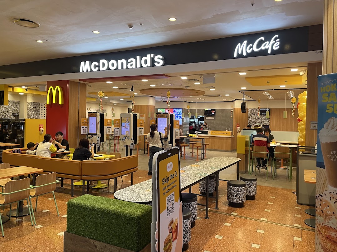 A bustling McDonald's interior featuring self-order kiosks, comfortable seating, and the McCafé section.