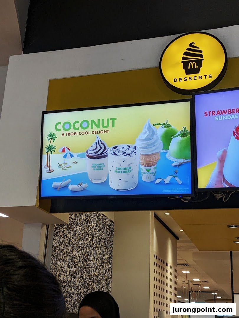 Digital menu boards at McDonald's showcasing tropical coconut desserts and a strawberry sundae.