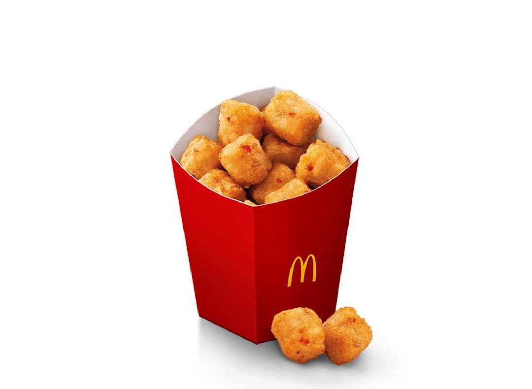 A red McDonald's box filled with golden-brown potato tots or nuggets, with two pieces outside.