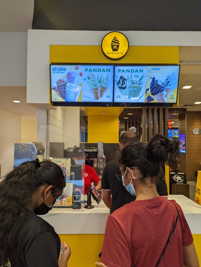 Customers ordering at a McDonald's dessert counter with digital menu boards displaying various sweet treats.