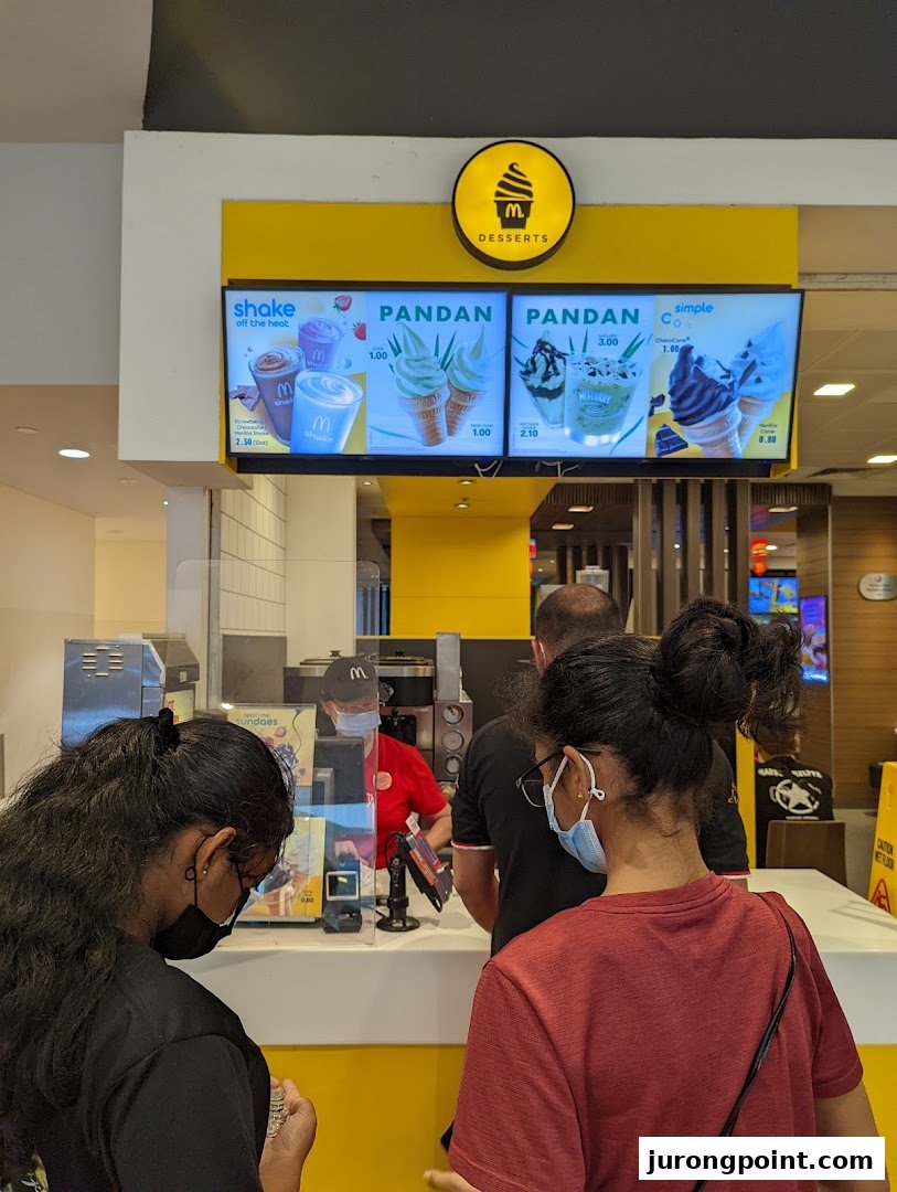 Customers ordering at a McDonald's dessert counter with digital menu boards displaying various sweet treats.