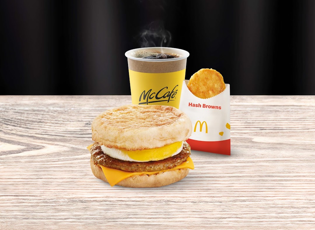 A McDonald's breakfast meal featuring a Sausage McMuffin, McCafé coffee, and hash browns.