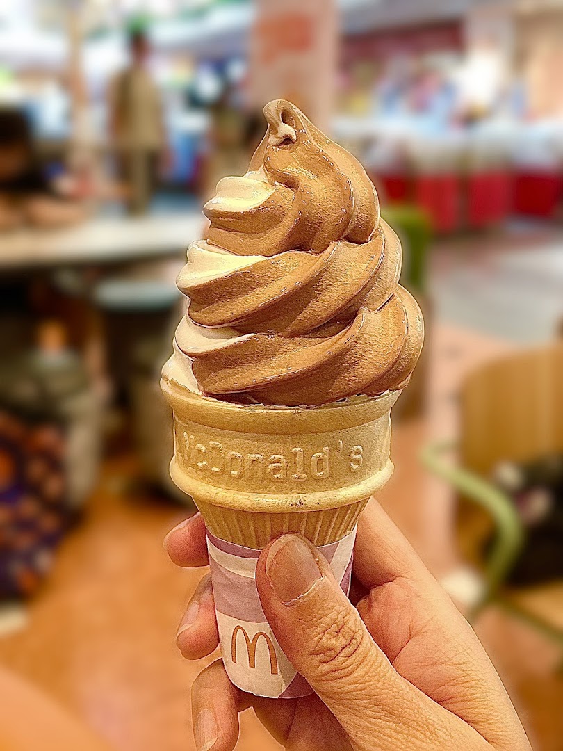 A hand holds a swirled chocolate and vanilla soft-serve ice cream cone from McDonald's.