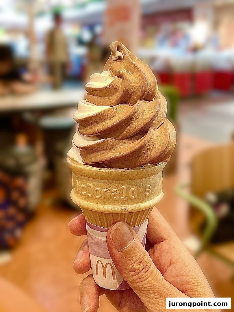 A hand holds a swirled chocolate and vanilla soft-serve ice cream cone from McDonald's.