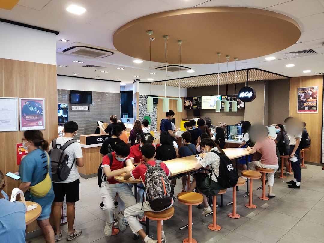 A bustling McDonald's interior with customers ordering and dining at tables and counters.