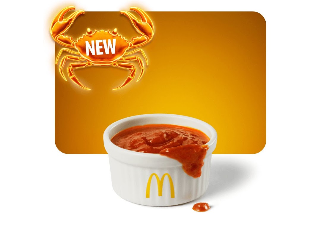 An advertisement featuring a glowing crab graphic with 'NEW' and a McDonald's sauce cup.