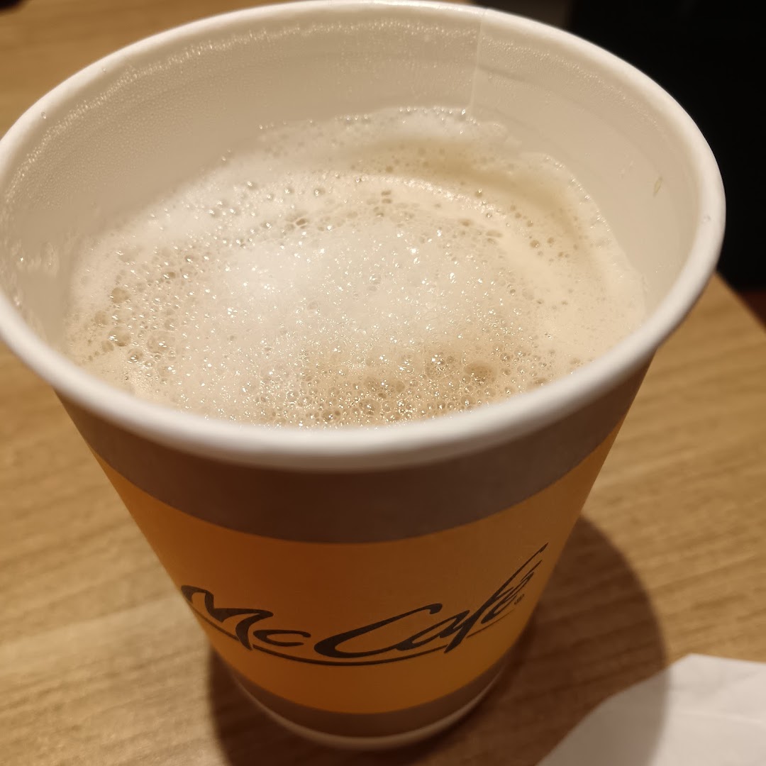 A close-up of a McCafe coffee cup filled with frothy coffee, resting on a wooden table.