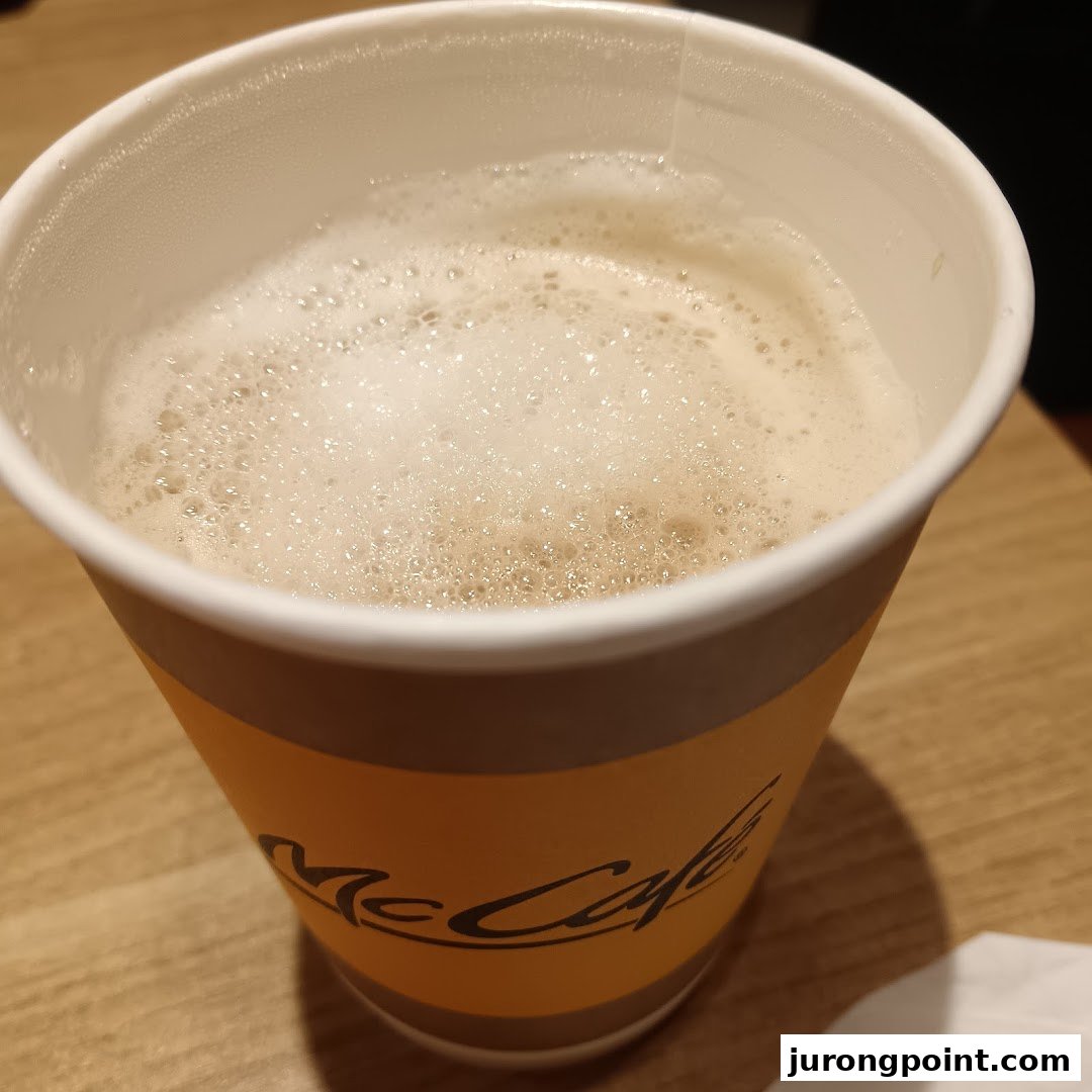 A close-up of a McCafe coffee cup filled with frothy coffee, resting on a wooden table.