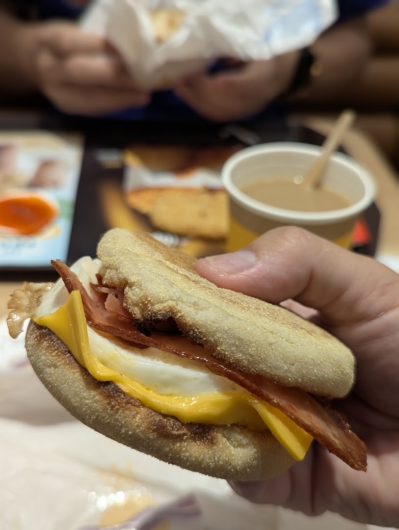 A hand holds a delicious McDonald's breakfast sandwich with egg, cheese, and bacon, alongside a coffee.