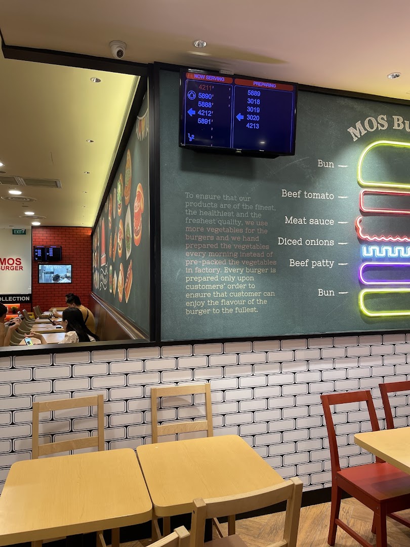 Interior view of MOS Burger showing seating, a large wall graphic detailing burger ingredients, and a queue display.