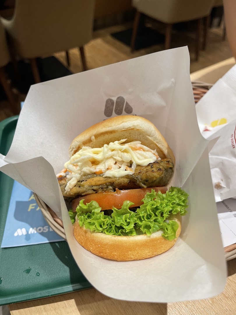 A close-up of a MOS Burger with fresh lettuce, tomato, and a patty topped with coleslaw.