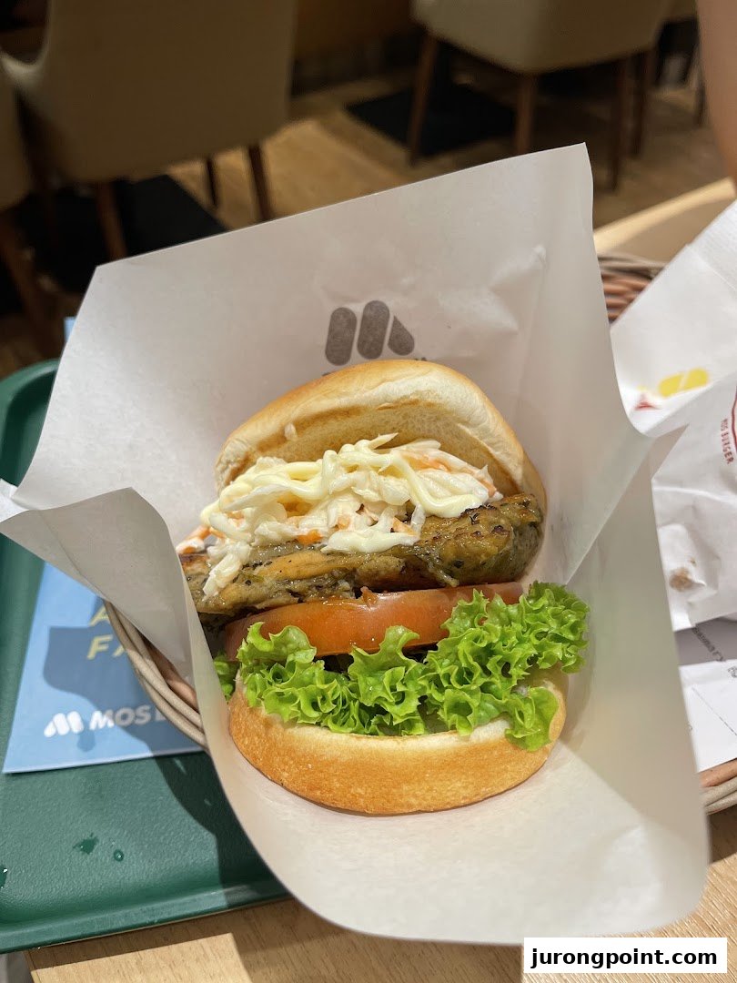 A close-up of a MOS Burger with fresh lettuce, tomato, and a patty topped with coleslaw.