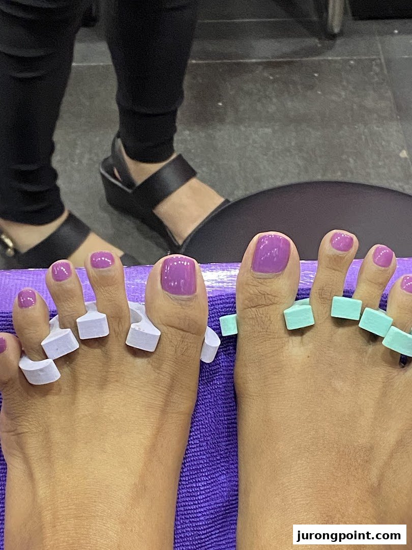 Close-up of feet with freshly painted purple toenails and toe separators during a pedicure.