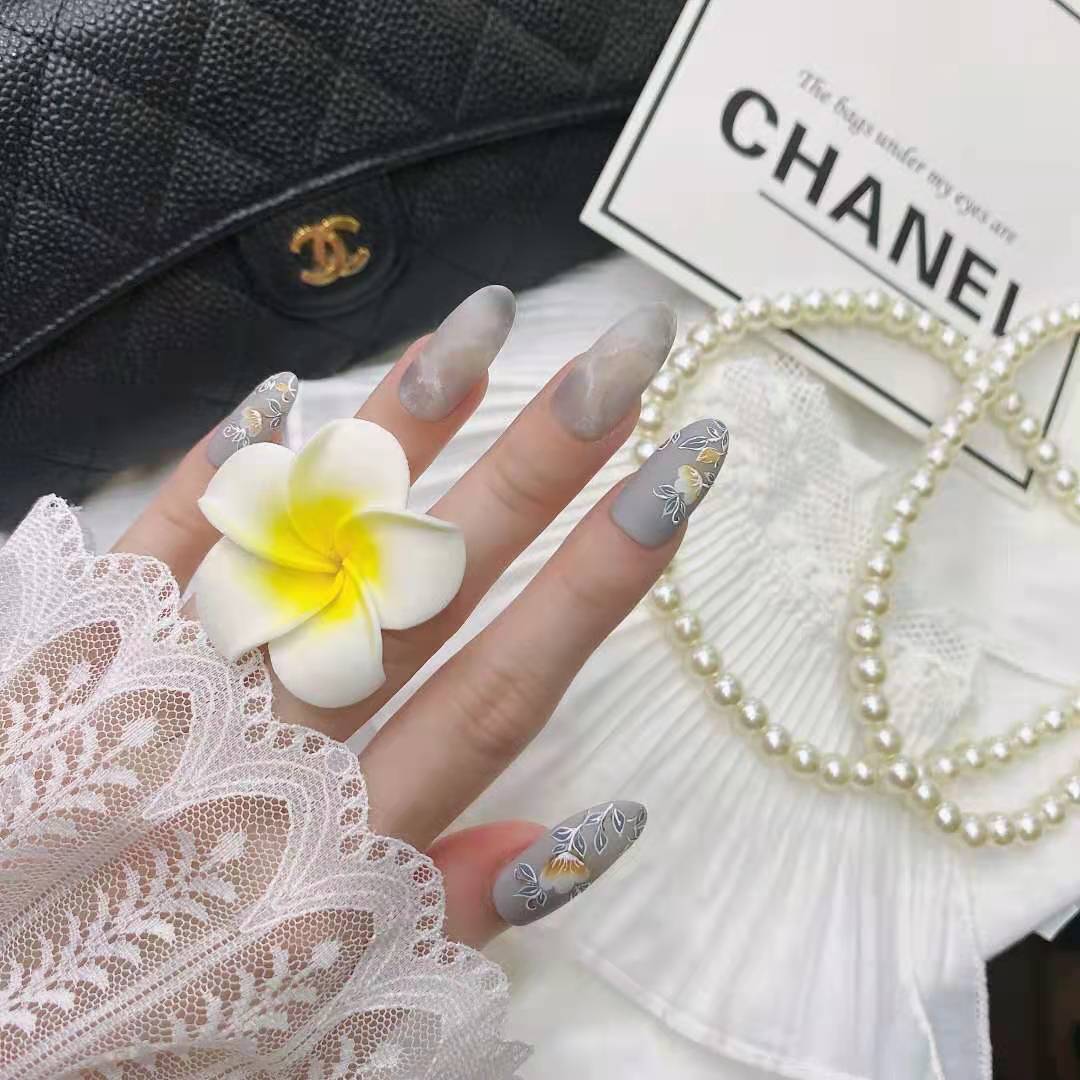 A hand displays long, stylish nails featuring intricate floral designs and subtle marble effects.