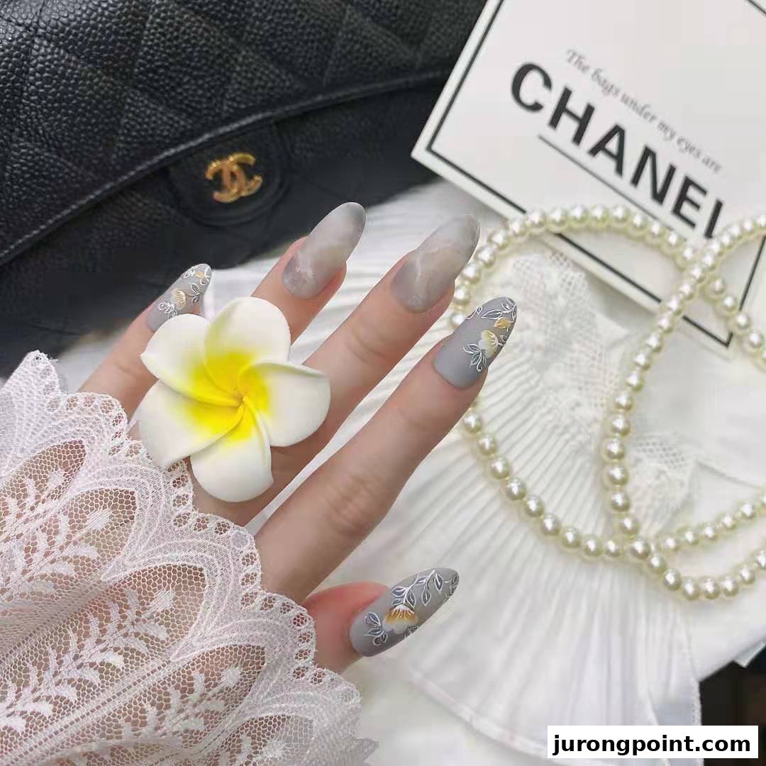 A hand displays long, stylish nails featuring intricate floral designs and subtle marble effects.