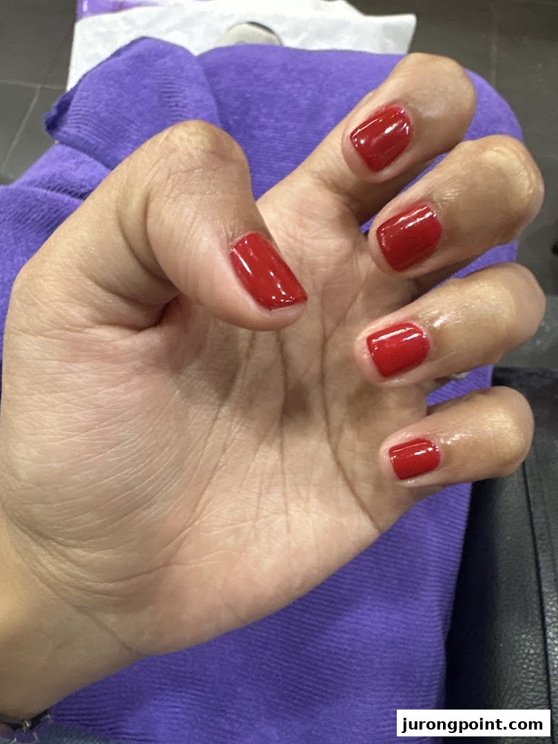 A hand showcasing freshly painted red nails, highlighting a service from Nail Palace.