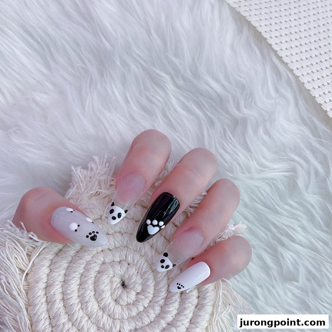 A hand displays long, clear and opaque nails adorned with cute panda faces and paw print designs.