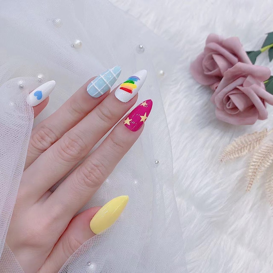 A hand displays vibrant, stiletto-shaped nails with diverse, playful designs including a rainbow and stars.