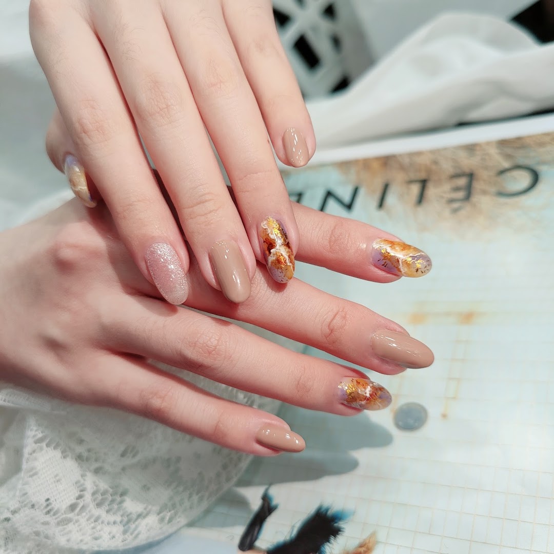 Close-up of hands showcasing elegant nail art with nude polish, glitter, and gold foil accents.