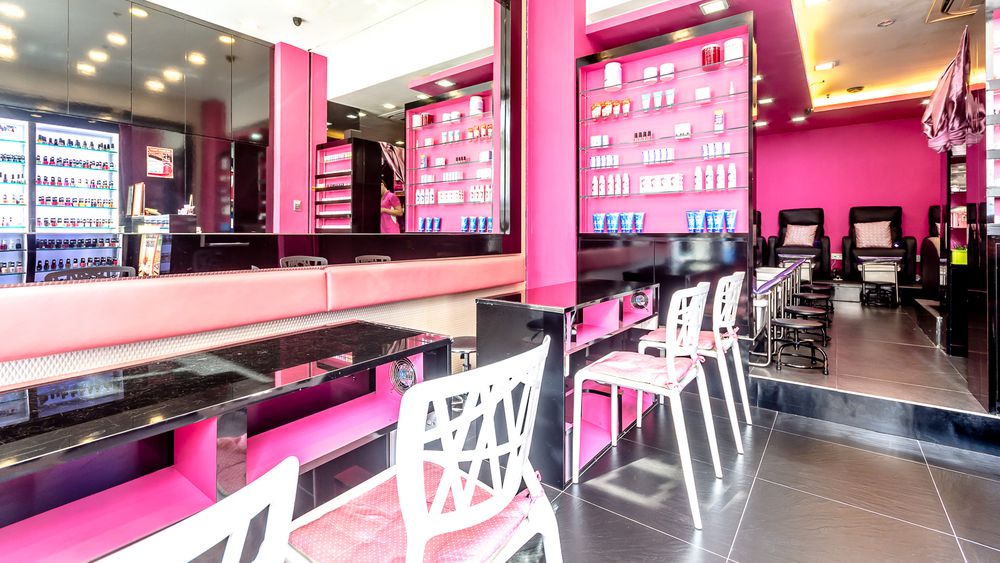 Vibrant pink and black interior of a nail salon with manicure stations and pedicure chairs.