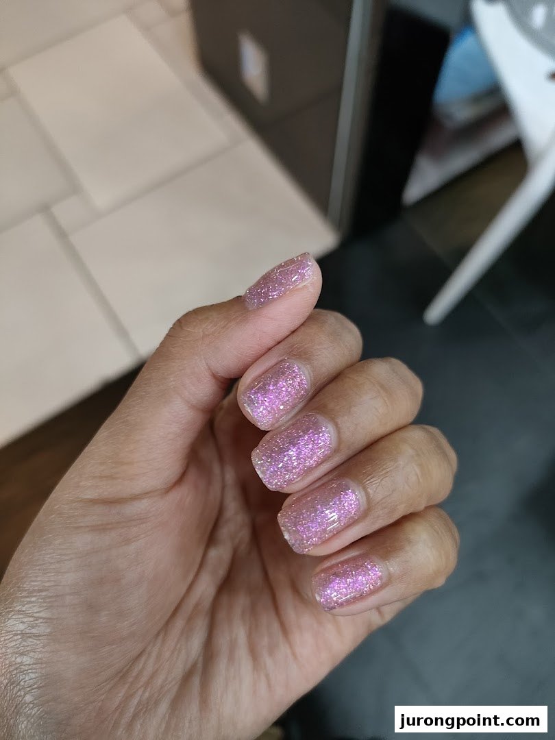 A hand showcasing freshly done nails with sparkling pink glitter polish.
