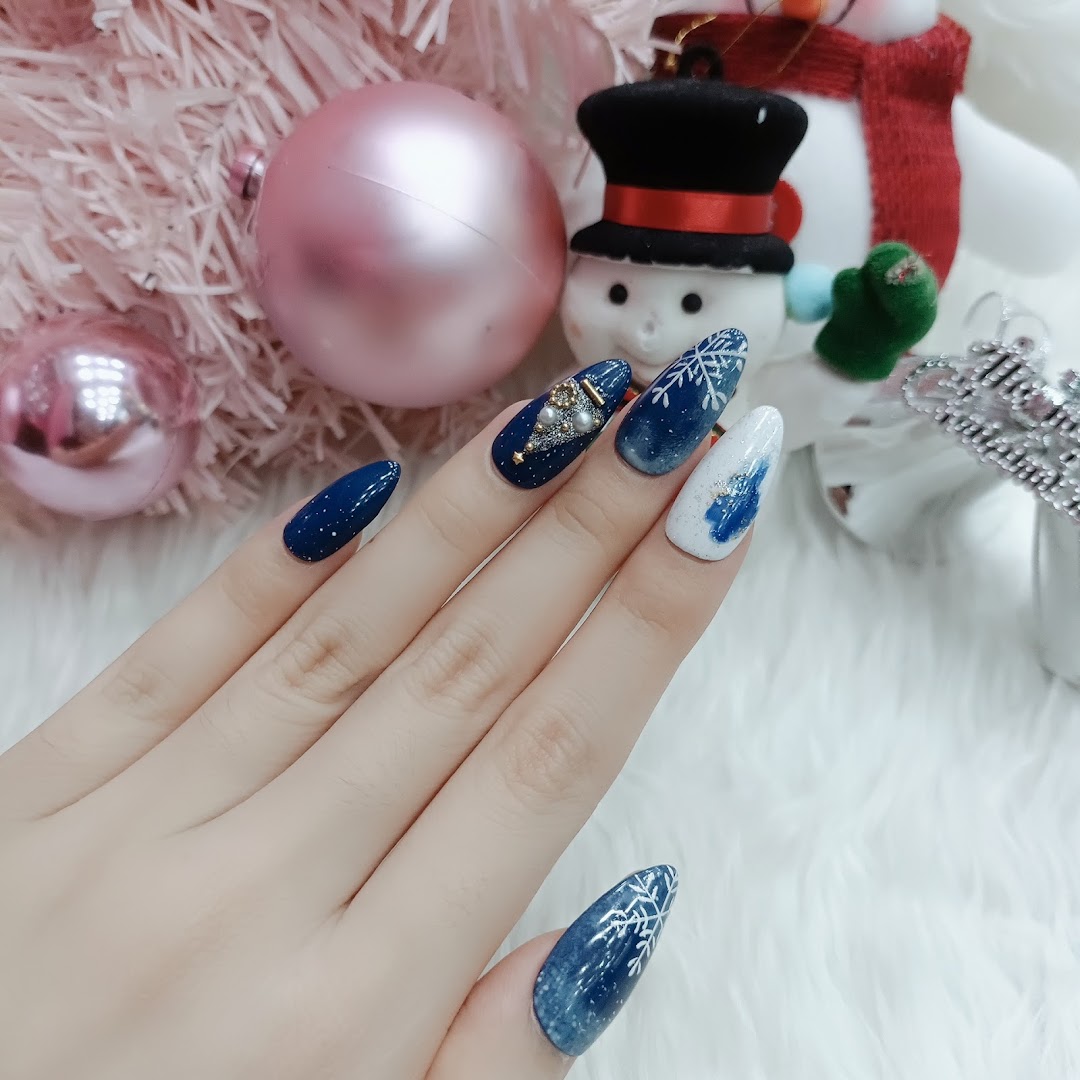 A hand showcases festive blue and white Christmas-themed nail art with snowflakes and a tree design.