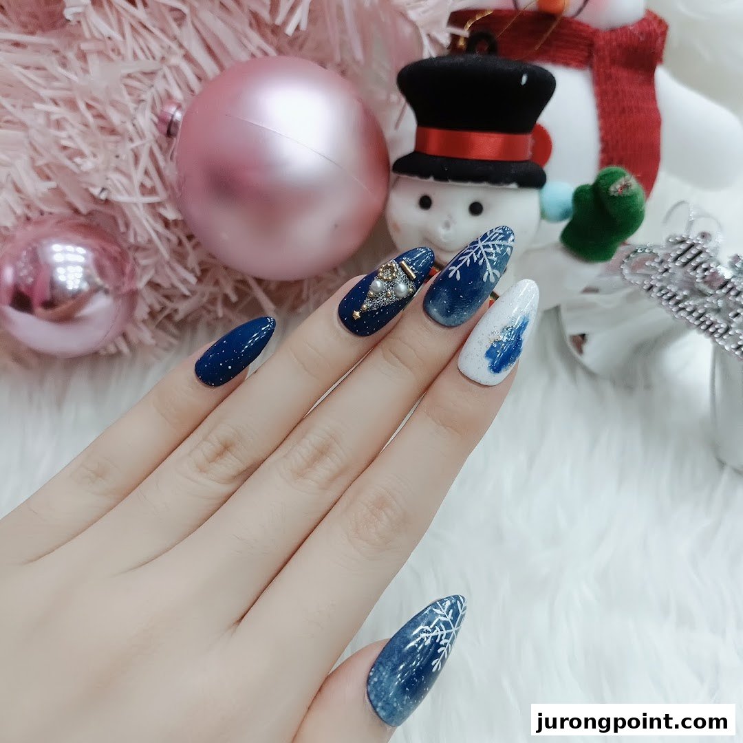A hand showcases festive blue and white Christmas-themed nail art with snowflakes and a tree design.