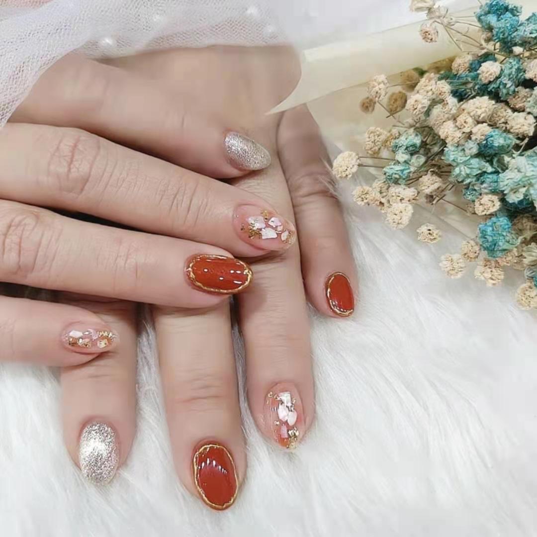 Close-up of hands showcasing intricate nail art with red, gold, and glitter designs.