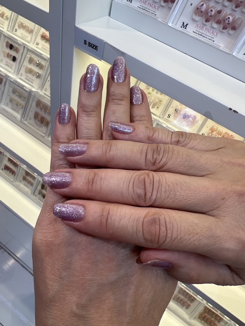 Close-up of hands showcasing sparkling purple glitter nail polish, with nail products in the background.