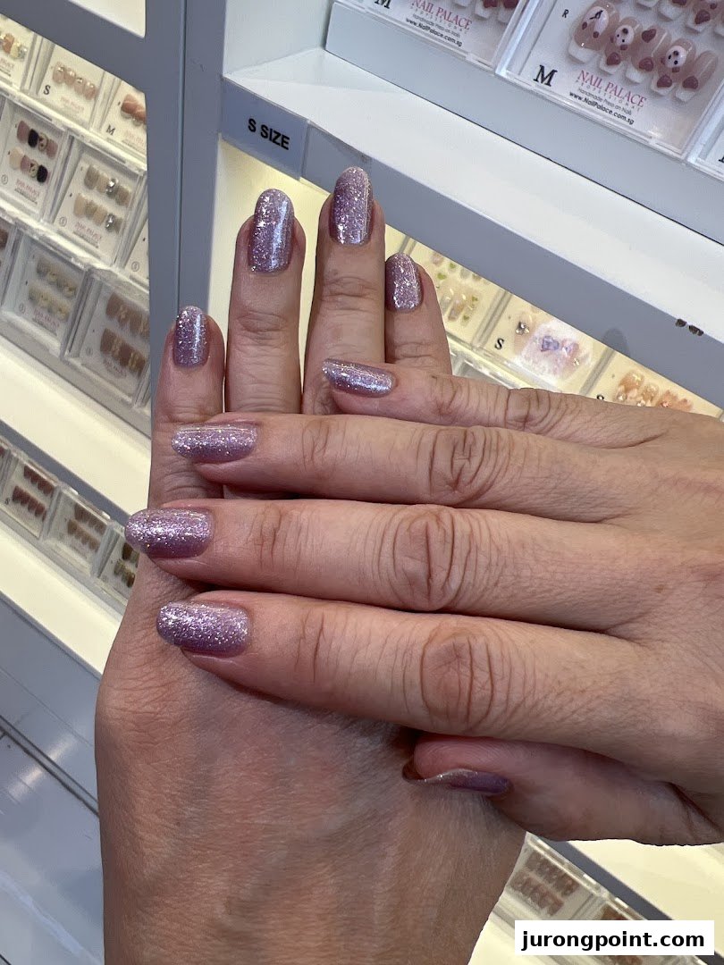 Close-up of hands showcasing sparkling purple glitter nail polish, with nail products in the background.