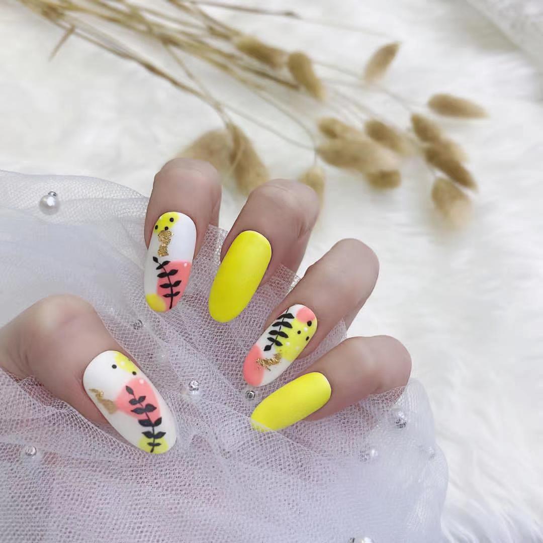 A hand showcasing vibrant yellow and artistic floral nail designs with gold accents.