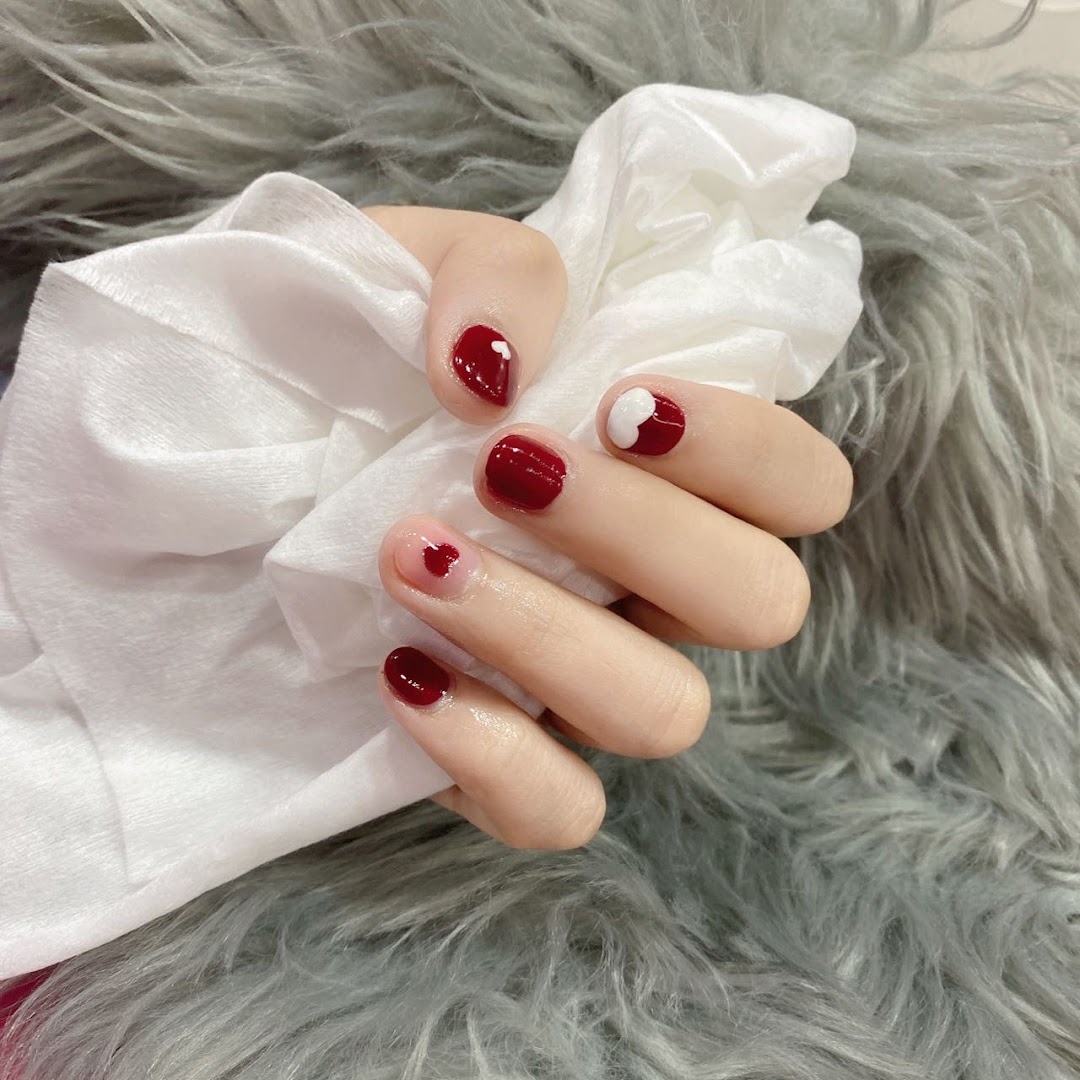 A hand showcasing red and pink nail polish with delicate heart designs on a furry background.