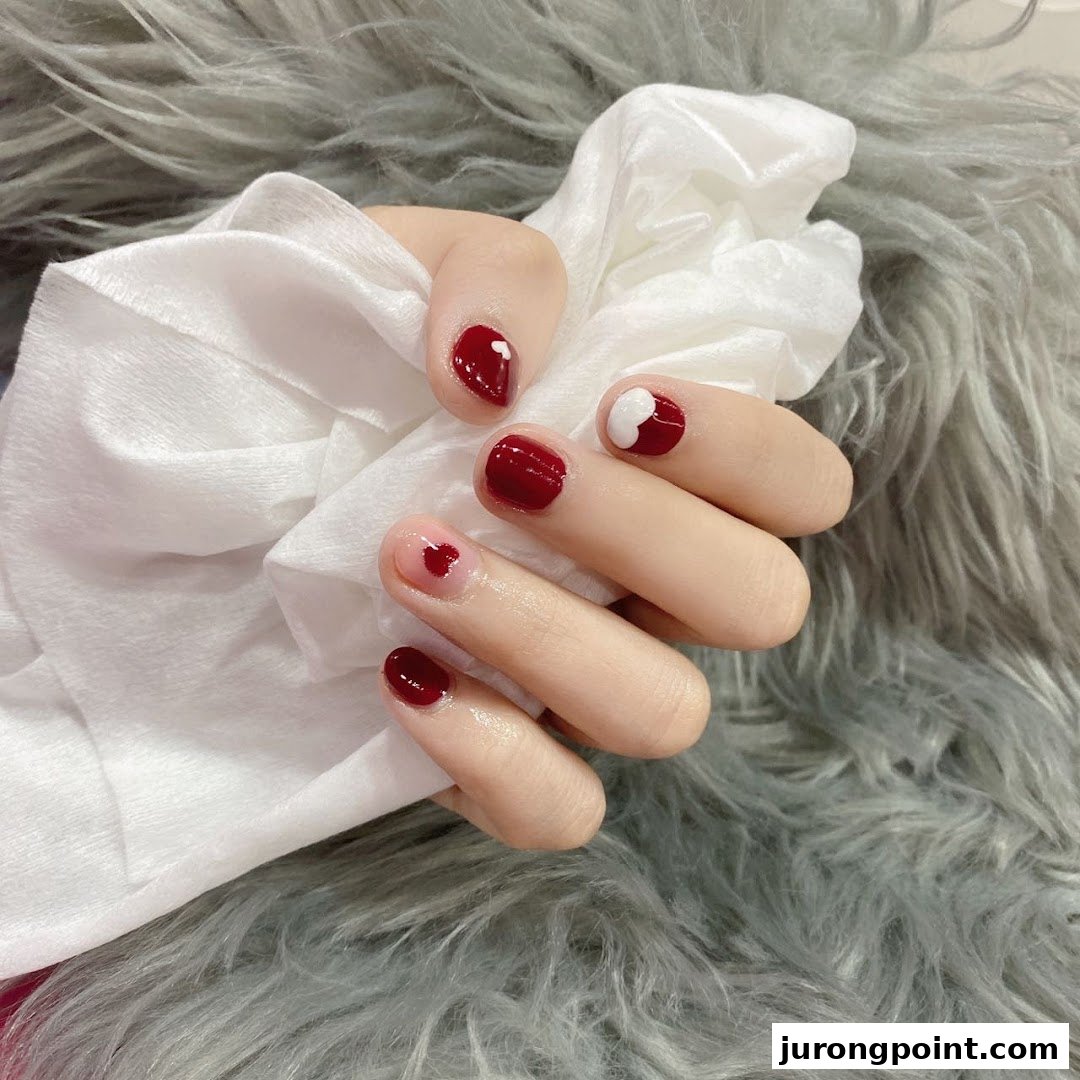 A hand showcasing red and pink nail polish with delicate heart designs on a furry background.