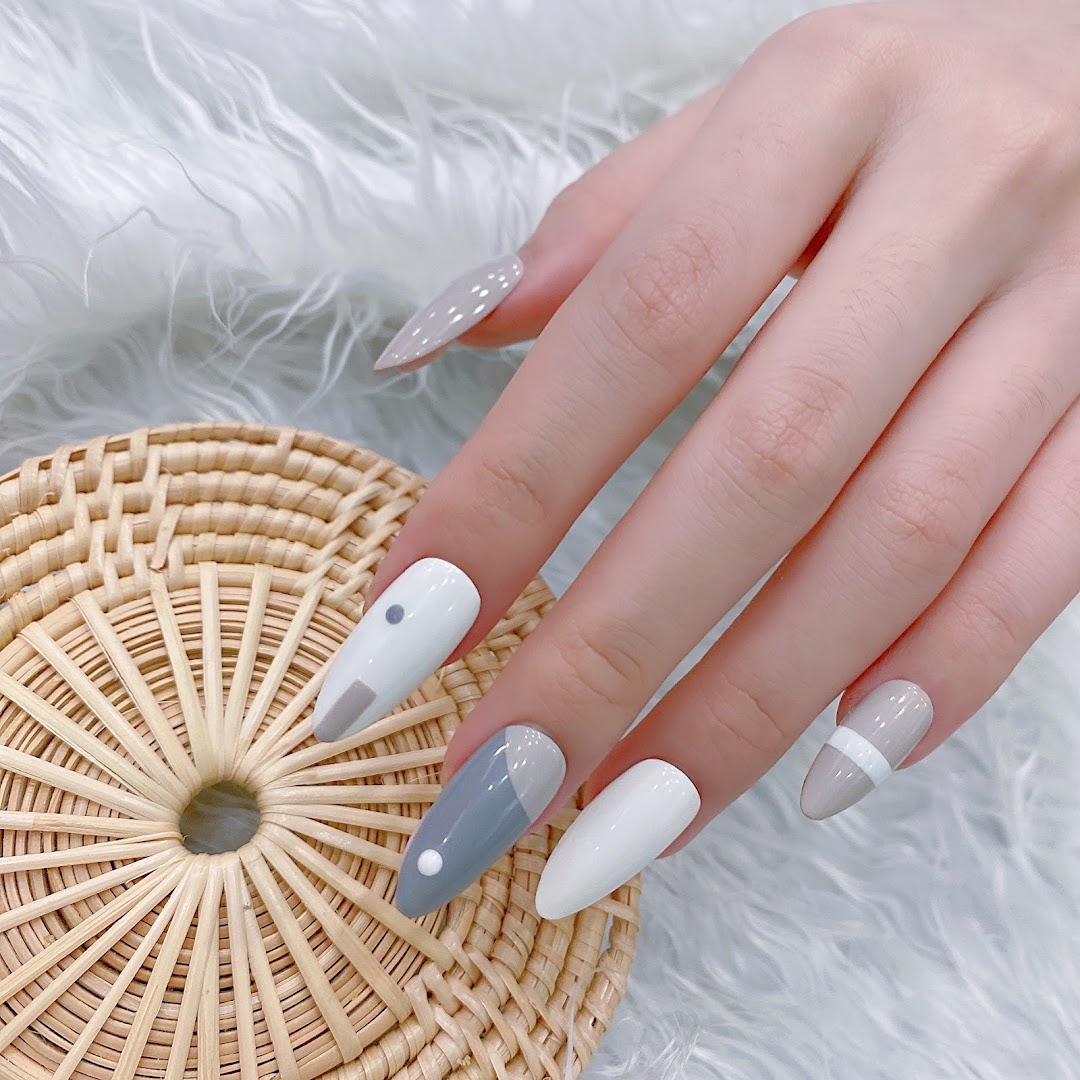 A hand showcasing modern nail art with grey, white, and beige geometric designs on a textured background.