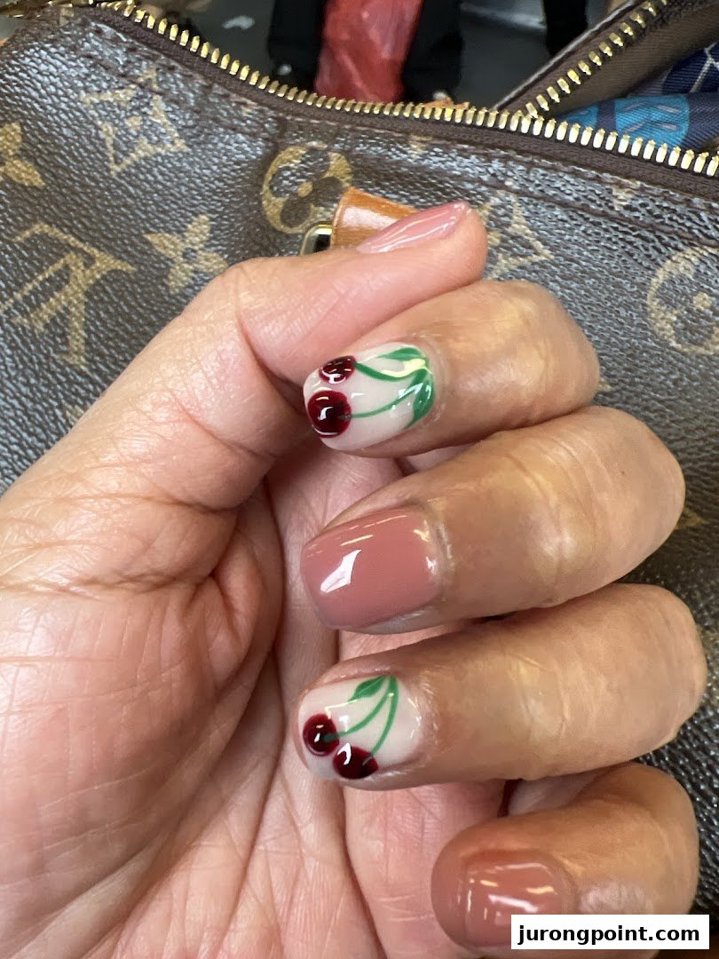 Close-up of a hand showcasing freshly manicured nails with cherry and solid pink designs.