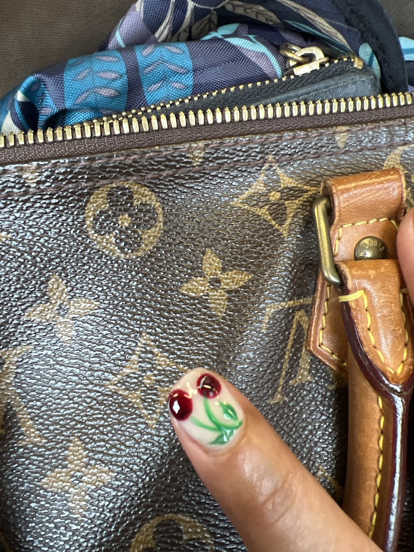 A close-up of a finger showcasing a vibrant cherry-themed nail art design against a textured background.