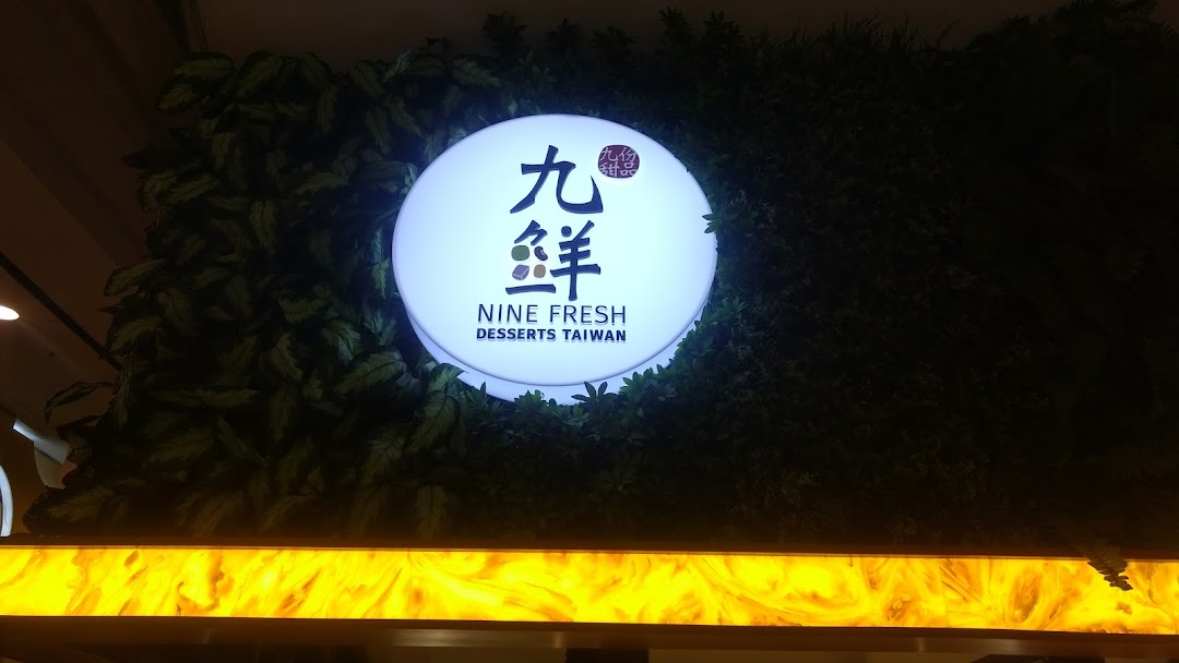An illuminated circular sign for Nine Fresh Desserts Taiwan set against a green artificial foliage wall.